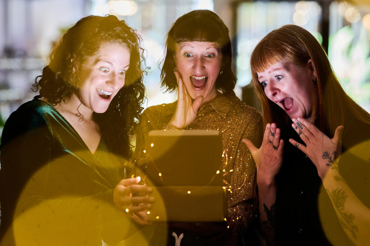 Trois femmes ouvrent une boîte lumineuse, les yeux et la bouche grands ouverts de surprise